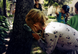 Dziewczynka ogląda korę drzewa przy użyciu lupy.